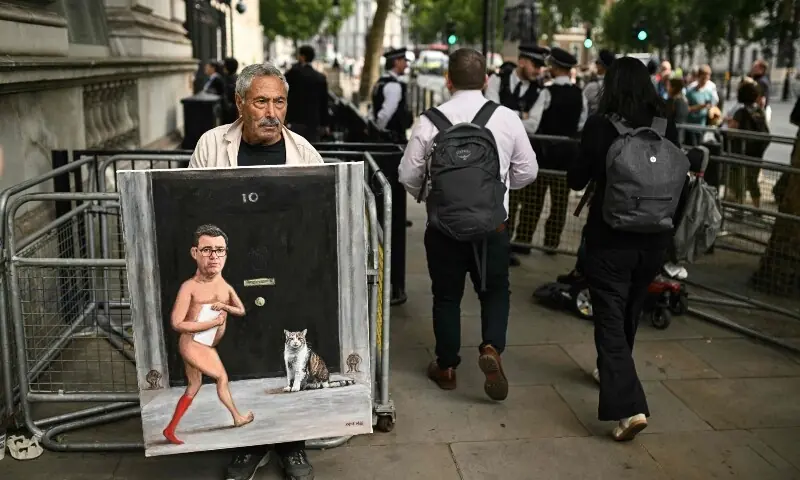 Political satire artist Kaya Mar (L) holds up a painting with a caricature of Britain’s incoming Prime Minister Andy Burnham and ‘Larry the Cat’ near Downing Street in central London on July 20, 2026, ahead of Burnham’s arrival as the country’s new leader. —AFP