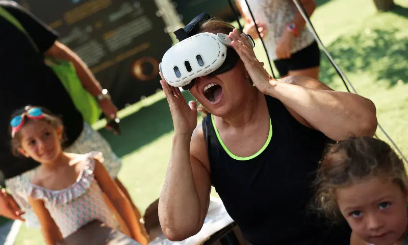 Angela Cordoba reacts as she wears virtual reality goggles next to her grandchildren, Gadea, 3, and Giulia, 6, as they attend an eclipse watch party on the day of a total solar eclipse in Buitrago del Lozoya, Spain, August 12, 2026.