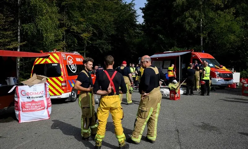 Firefighters gather near the Mobile Command Unit vehicle (R) and Fire Service Logistics Support vehicle (L) serving as a canteen in Baelen, near Eupen, eastern Belgium, as they prepare to tackle a wildfire burning in the Hautes Fagnes (High Fens) nature reserve on August 16, 2026. — AFP