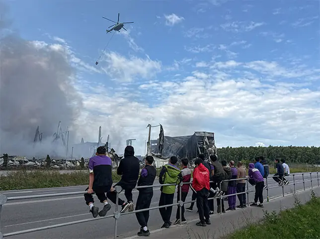 People watch as a water-bombing helicopter flies above the burning warehouses after a Ukrainian drone attack in Moscow region.&mdash;Reuters