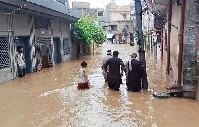 People walk through a flooded street in Safdarabad in Rawalpindi’s Pirwadhai area on Monday. — White star