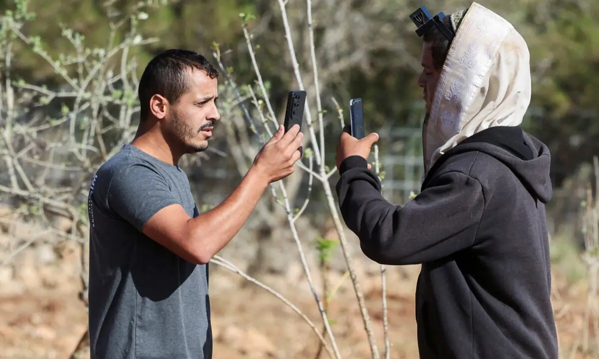 Yousef Hassan (L), whose house was encircled by militant settlers and later taken over by the military, films an Israeli settler (R) who entered the property of Palestinian-American Loui Ridi, in Qusra, Israeli-occupied West Bank on August 18, 2026. &mdash;Reuters