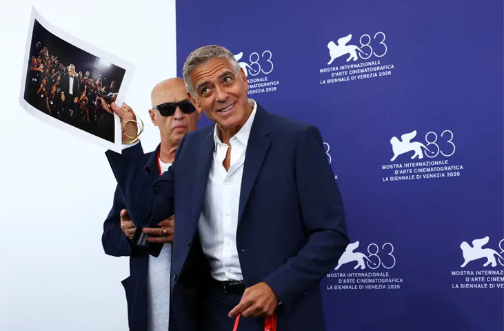 GEORGE Clooney holds up a photograph of himself from a previous festival, along with a photographer’s accreditation badge, during a media event in Venice.—Reuters