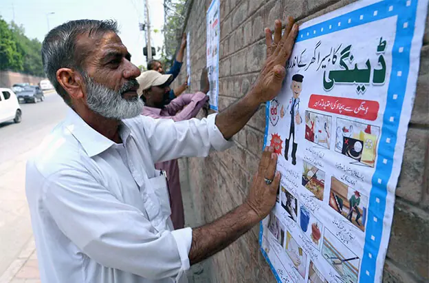 Health workers paste dengue awareness posters on Sher Shah Suri Road, Peshawar, on Thursday. — APP
