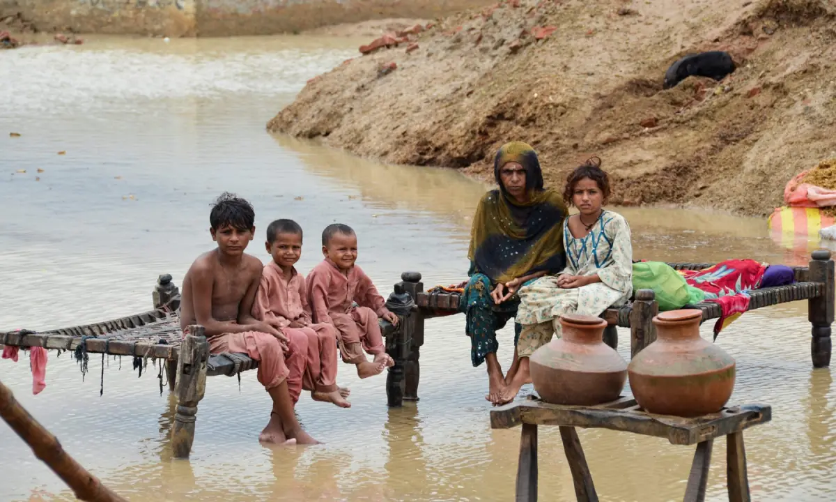 A woman and children sit on rope beds amidst rain waters besides their damaged house following rains and floods during the monsoon season in Dera Allah Yar, district Jafferabad, Balochistan, Pakistan, on August 25, 2022. — Reuters