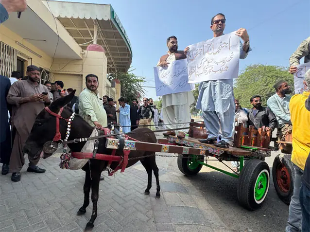 PTI lawmakers stand atop a donkey cart outside the main entrance of the Sindh Assembly to protest against fuel price hikes.—Dawn