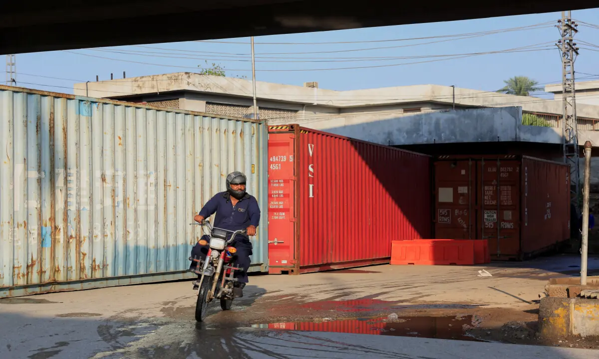 A man on a motorbike rides past a wall of shipping containers used to block access to the Red Zone in Peshawar on October 12, 2026. &mdash; Reuters