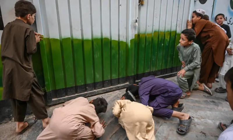 Children try to peek through the sealed entrance of school a day after its roof collapsed killing several students in Peshawar on October 16, 2026. — AFP