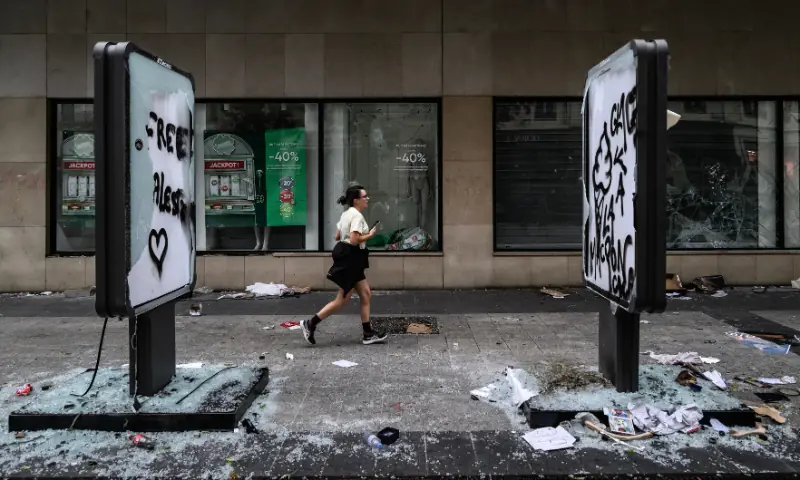 A pedestrian runs past damages and a broken frontage windows of a shop a day after riot and looting following a nationwide protest against the “high cost of living”, in Lyon central-eastern France on October 18, 2026. — AFP