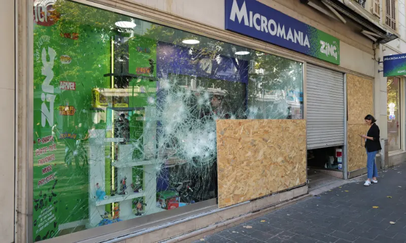 A woman stands next to a damaged Micromania-Zing video game retail shop at Jean-Medecin avenue in Nice, southeastern France on October 18, 2026, after a nationwide protests against the “high cost of living”. — AFP