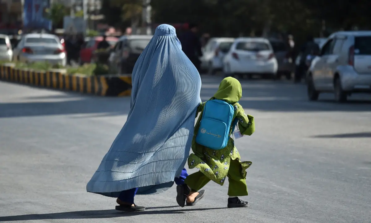 This photograph taken on October 20, 2026 shows a burqa-clad woman with a girl crossing a street in Sheberghan in Afghanistan’s Jawzjan province. — AFP