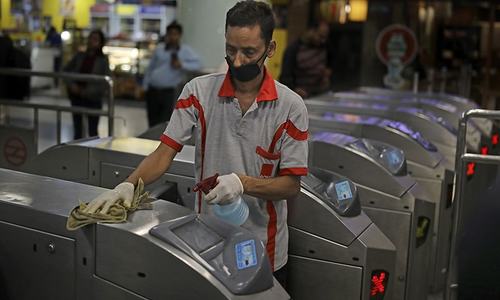 A worker disinfects the gates as a precaution against COVID-19 at a metro station in New Delhi on March 13. — AP