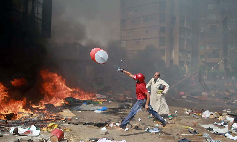 A supporter of the Muslim Brotherhood and Egypt's ousted president Mohamed Morsi throws a water container onto a fire during clashes with police in Cairo on August 14, 2013, as security forces backed by bulldozers moved in on two huge pro-Morsi protest camps, launching a long-threatened crackdown that left dozens dead. — Photo by AFP