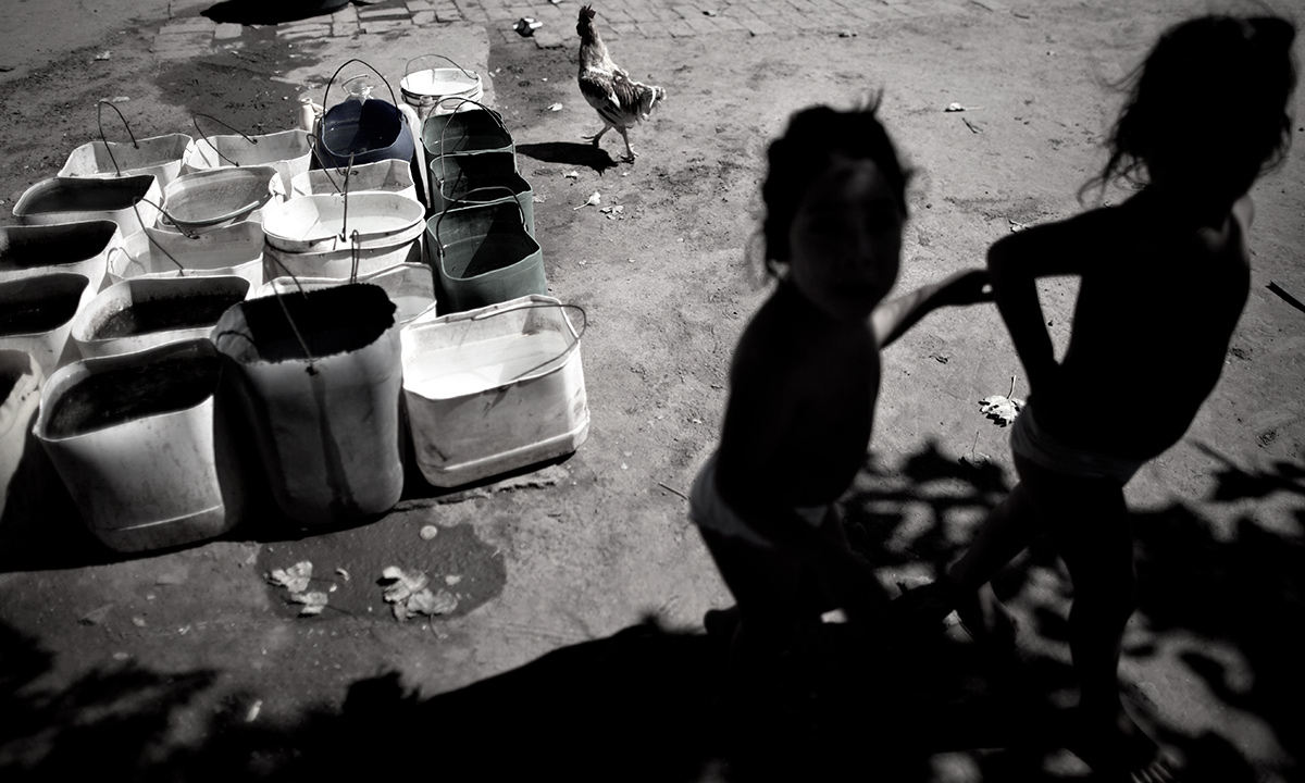 Erika, left, and her twin sister Macarena, who suffer from chronic respiratory illness, play in their backyard near recycled agrochemical containers filled with water that is used for flushing their toilet, feeding their chickens and washing their clothes, near the town of Avia Terai, in Chaco province, Argentina. - AP Photo