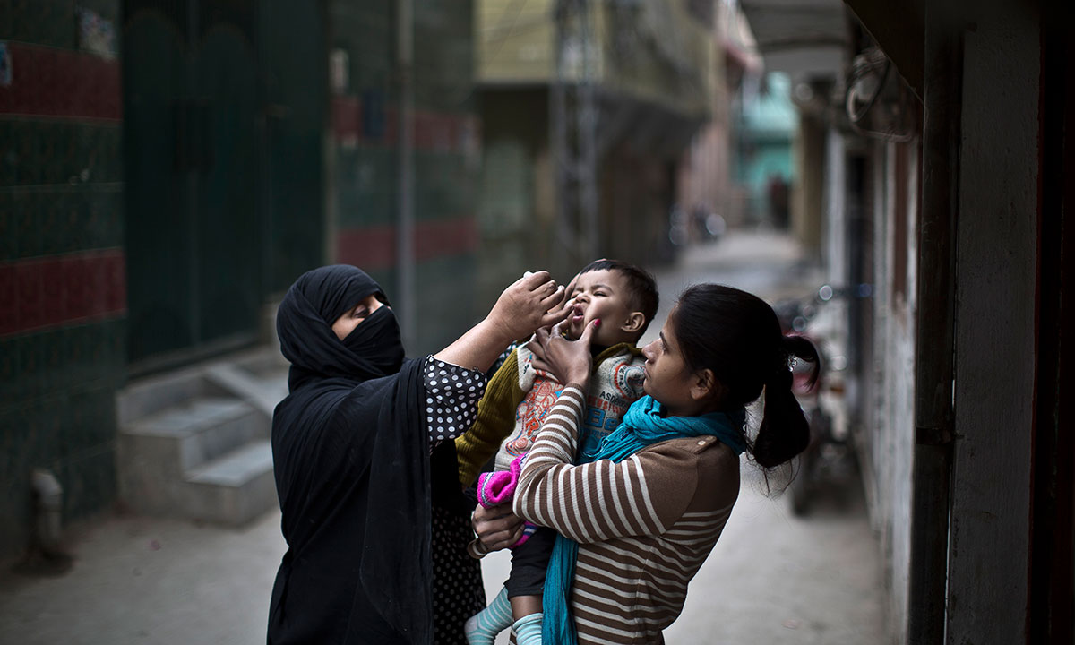 A Pakistani woman, right, holds her nephew to be vaccinated against polio by Mariam Jabir, 32, while going house to house checking on children who need the vaccine, in Rawalpindi, Pakistan, Tuesday, Jan. 21, 2014. Gunmen in a pair of attacks minutes apart struck two teams of polio workers in the southern city of Karachi, killing three members of the teams and wounding a fourth before fleeing, police said. Police official Pir Mohammad Shah said two female and a male worker were killed in the attacks in Karachi, the