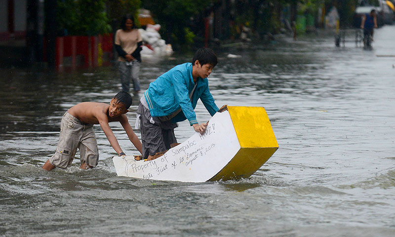 Children use a makeshift "boat" to cross a flooded street in Manila on August 19, 2013 as heavy rains hit the Philippine capital. Heavy rain forced all schools, government offices and the stock exchange to close on August 19, as waist-deep water flooded parts of the city.   AFP PHOTO / NOEL CELIS