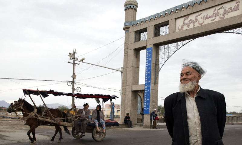 A bearded elderly Uighur man uses a plastic bag over his doppa to cover from a light rain in the city of Kuqa in western China