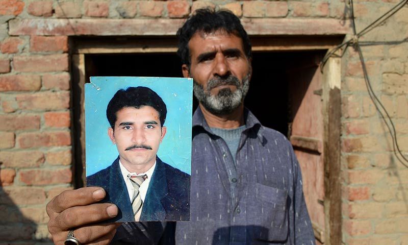 The father of Mohammad Irfan, who was sentenced to death for drug trafficking in Saudi Ariabia, Haji Abdul Haq, poses with a picture of his son in Sargodha. — AFP