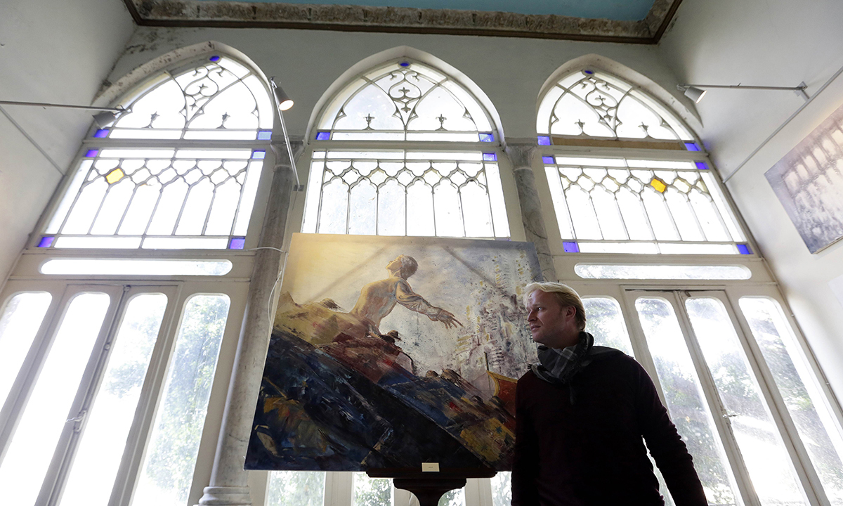 British painter Tom Young poses next to one of his paintings during an exhibition in Ras Beirut's landmark Rose House. &mdash; AFP