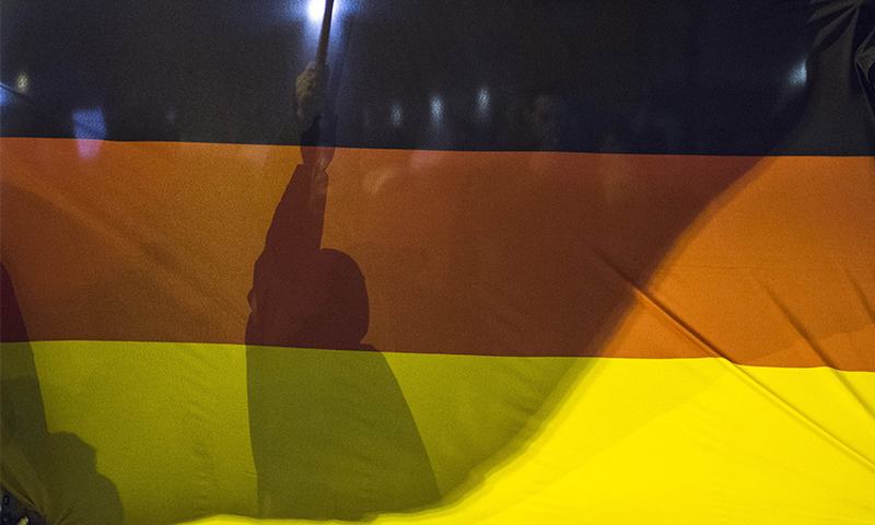 A demonstrator holds a flag behind a giant national flag during a rally by the mounting right-wing populist movement Pegida on January 5, 2015 in Berlin.--AFP