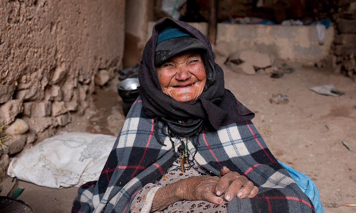 A woman smiles as she warms herself near a fire at her home in Tilmi village.