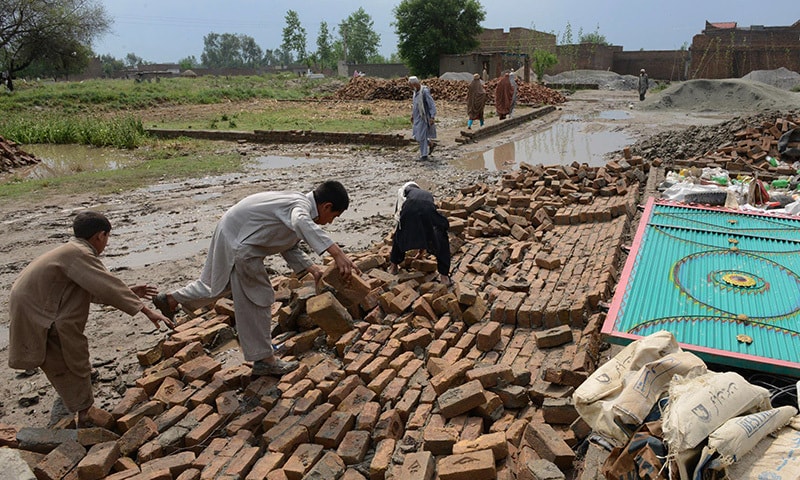 Pakistani residents collect bricks after their house collapsed following heavy rain and winds in Peshawar on April 27, 2015. —AFP