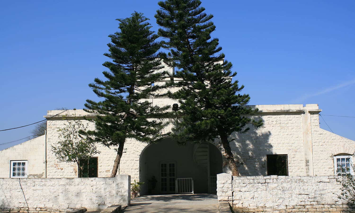 Two tilted pine trees overshadow the front entrance of Pathar Kothi.