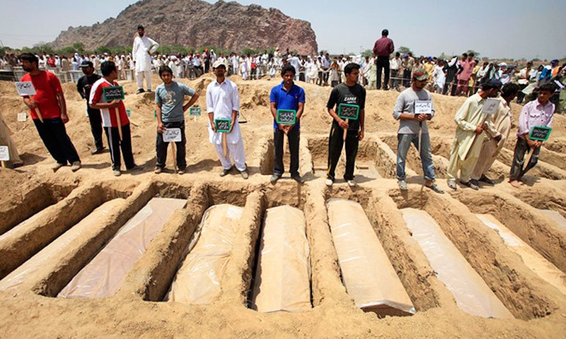 Members of the Ahmadi community hold the names of victims as they stand over their graves in on May 29, 2010. —Reuters