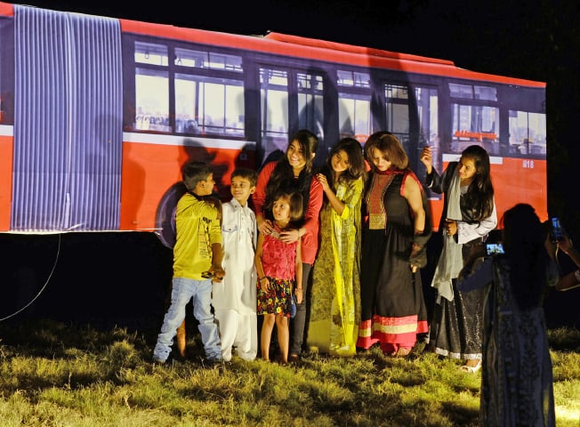 Families pose for a photograph next to a cut out of a metro bus in Islamabad on Wednesday. &mdash; Dawn