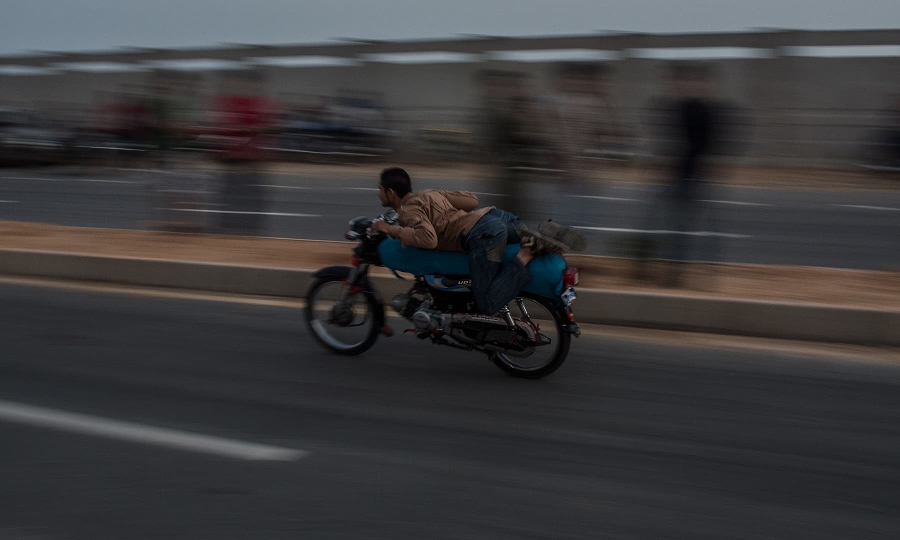 A biker lies flat on his motorcycle as he glides past spectators