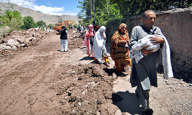 A family heading towards their destination while walking on a damaged road due to recent floods. — APP