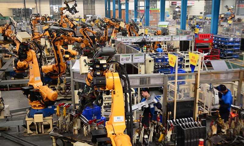 In this June 26, 2015 photo, workers assemble parts next to robot arms at an auto parts manufacture factory in Dafeng city in east China's Jiangsu province. &mdash;AP