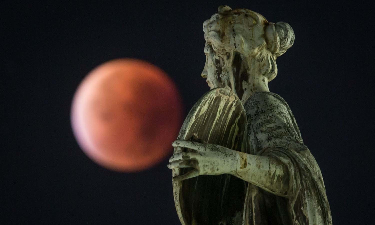 A so-called "blood moon" can be seen behind a statue during a total lunar eclipse in Frankfurt am Main, western Germany. — AFP