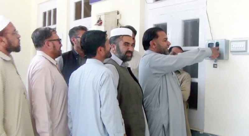 Staff members line up outside the DHQ hospital, Upper Dir, to register their attendance on a biometric machine. &mdash; Dawn