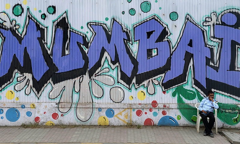 AN Indian security guard sits at the entrance of an underconstruction residential complex embellished with grafitti on its perimeter in Mumbai. &mdash; AFP