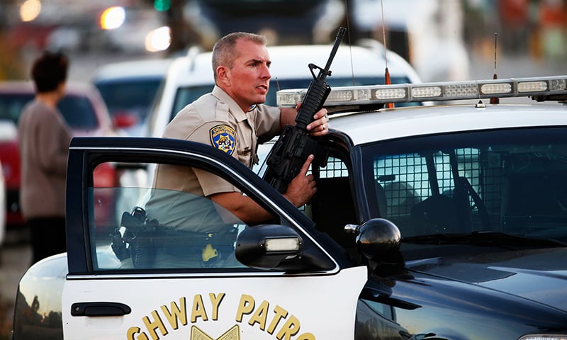 A California Highway Patrol officer stands with his weapon as authorities pursued the suspects in a shooting that occurred at the Inland Regional Center. -AFP