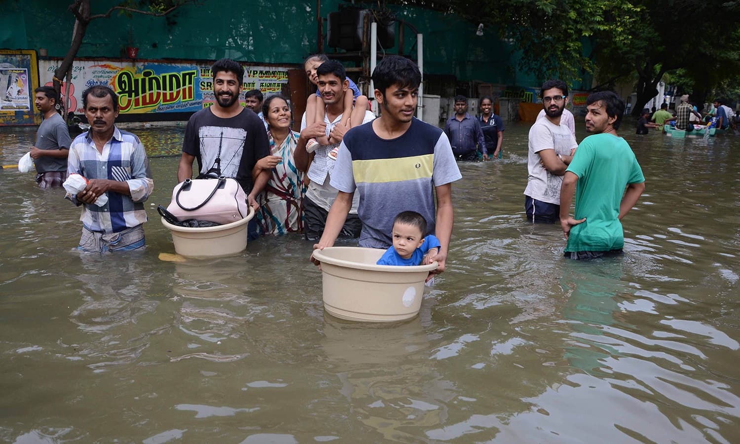 Indian residents carry children and possessions as they walk through floodwaters in Chennai on December 3, 2015. — AFP