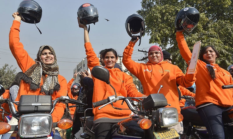 Participants of Women on Wheels (WOW) raise their helmets at the start of a rally in Lahore. ─AFP