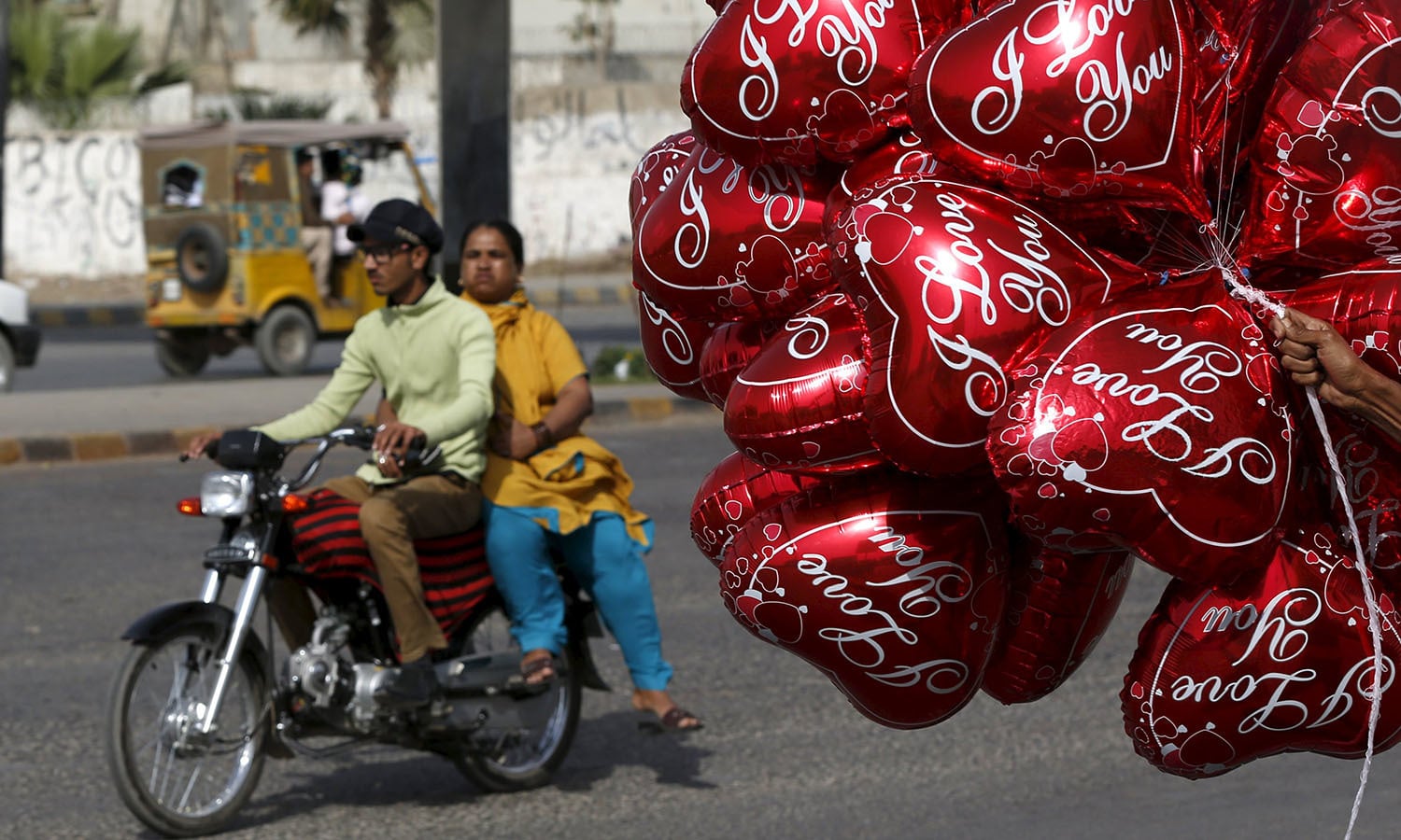 A couple on a motorcycle ride past a vendor selling heart-shaped balloons on Valentine's Day in Karachi.─Reuters