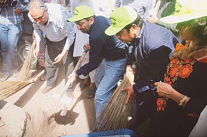 Senior deputy convener of the Muttahida Qaumi Movement Dr Farooq Sattar shovels earth out of the road with activists taking part in the clean-up drive on Thursday.&mdash;Online