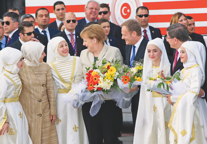 Nizip: German Chancellor Angela Merkel (centre) accompanied by EU Council President Donald Tusk (right) talks to young women at a refugee camp on Friday.—AP