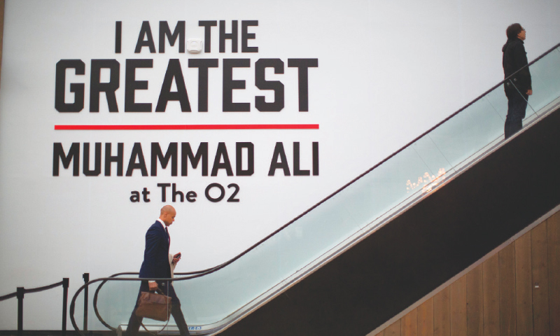 LONDON: Men pass a large sign by an escalator near the entrance of the ‘I Am The Greatest, Muhammad Ali’ exhibition on Saturday at the O2 arena, which hosts high-profile boxing fights.—AP