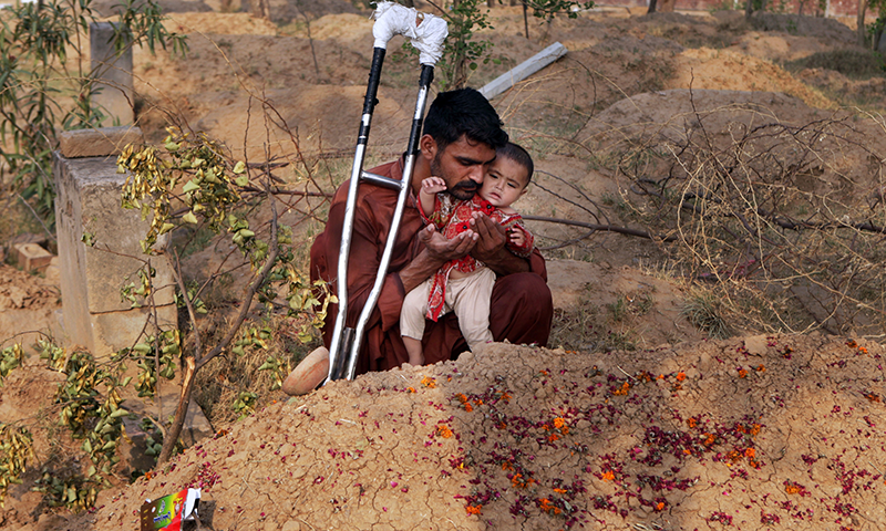 Mohammed Tofeeq holds his 10-month-old daughter while he prays at the grave of his wife Muqadas Tofeeq, who local police say was killed by her mother. — AP/File