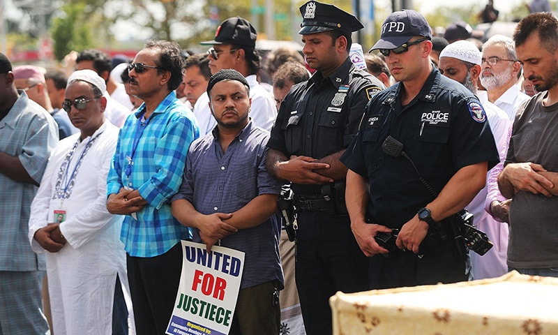 Police officers stand with muslims during a prayer for Imam Akonjee and his assistant.— AFP