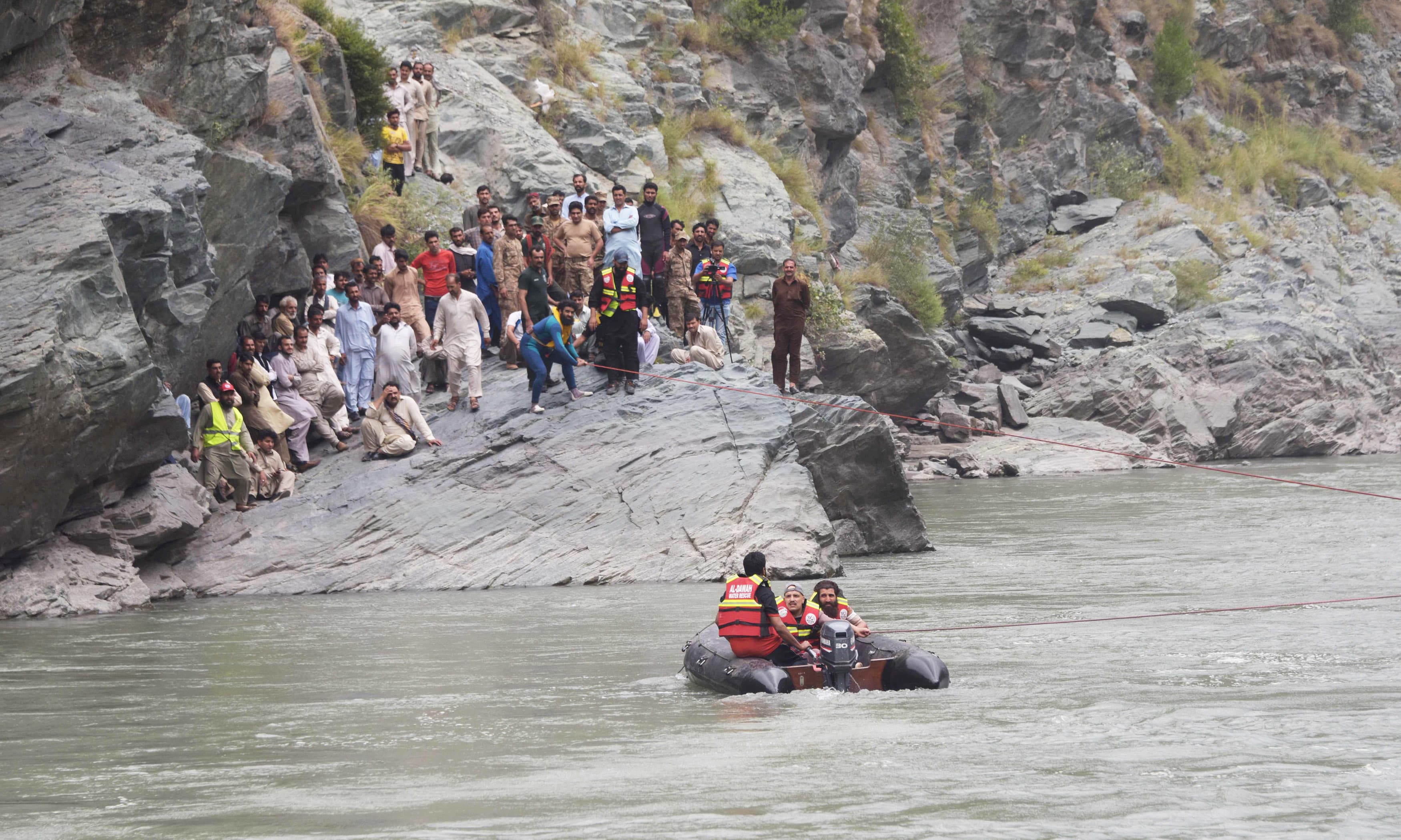 Rescuers use ropes attached to a crane to try to recover a bus that fell into a river in Nausehri. —AFP