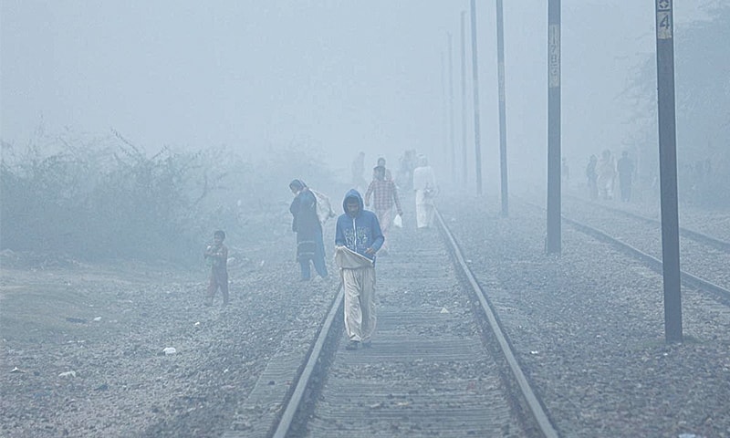 LAHORE: People cross the railway track in the Walton area during foggy weather on Sunday.&mdash;Online