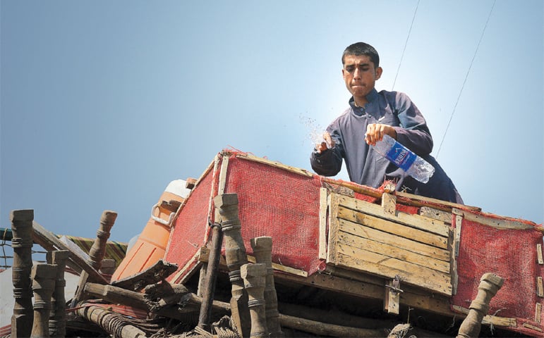 A refugee sprinkles water on chicken in a cage on top of a loaded truck as he leaves Chamkani Repatriation Centre, Peshawar &mdash; Photo by Shahbaz Butt/White Star