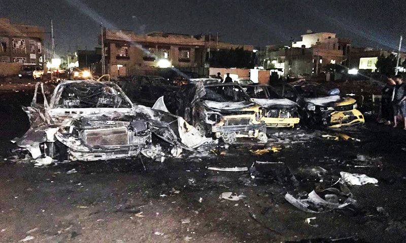 Civilians gather at the site of a car bomb in a used car dealer's parking lot in Baghdad.—AP