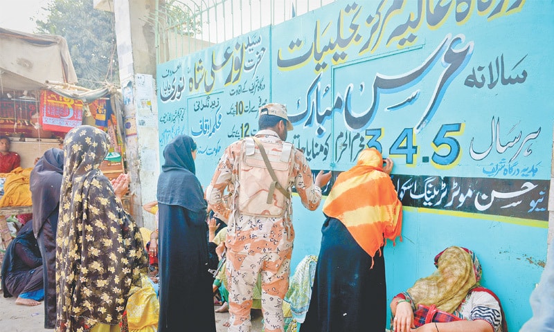 DEVOTEES gather outside the closed Noor Ali Shah shrine near Teen Hatti in Karachi on Friday as a Rangers&rsquo; trooper looks on.&mdash;White Star