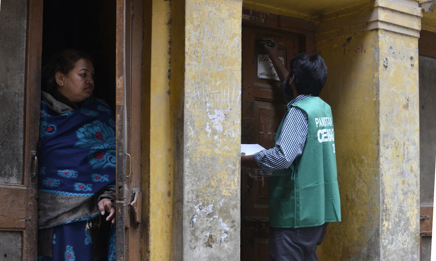 Another enumerator marks a house as a resident looks on during country's enormous, politically charged census. ─AFP